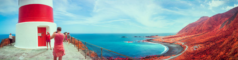 A wide panorama of the view from the top of the lighthouse; Sam is taking a photo of Britt infront of it.