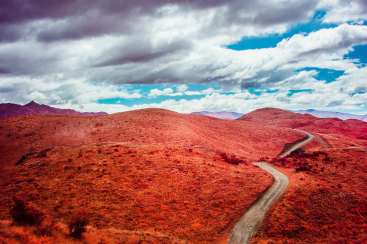 Rolling red hills, partly cloudy, a winding dirt road.