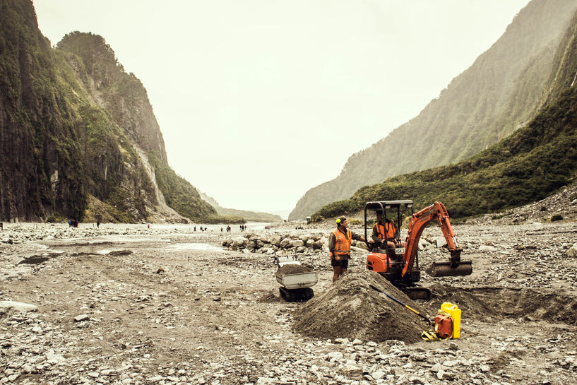 Workers in a mini-backhoe doing a tiny amount of earth moving in the middle of a vast glacial valley.