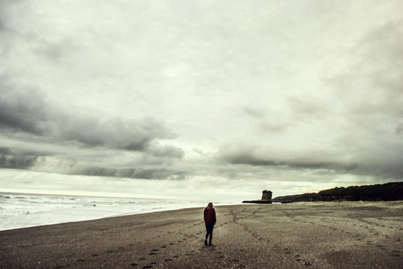 Moody photo of tiny, dark Britt on a wide cloudy beach.