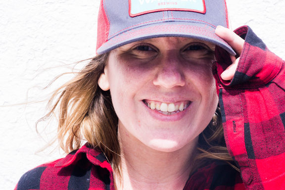 Close-up of Britt, smiling from ear to ear and clutching the brim of her hat.