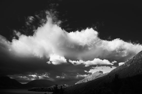 Towering bright white clouds on a black sky, lakes and a mountain.
