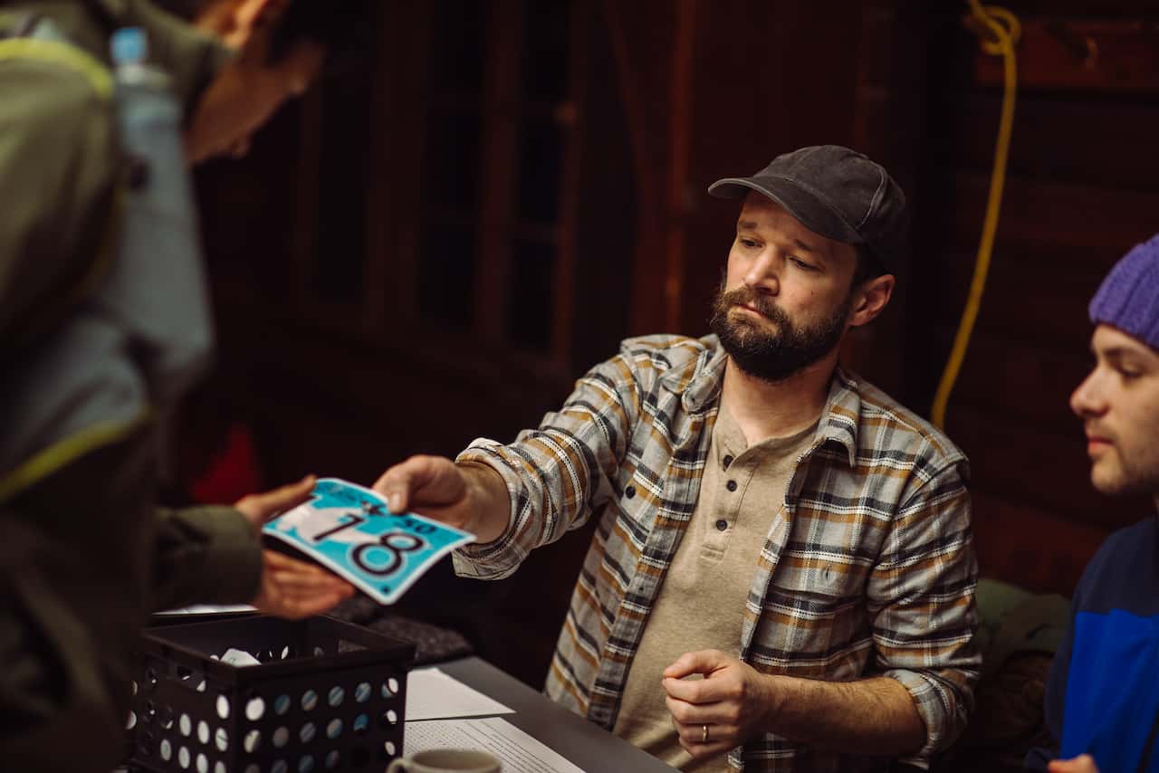 Me, in a flannel, sitting behind a table, handing a racer their bib. I’m wearing a serious expression.