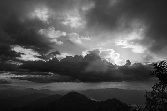 Dramatic clouds at sunset, above some dark, moundy-looking mountains